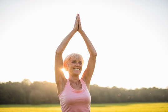 Smiling senior woman doing yoga on rural meadow at sunset