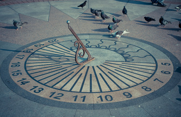 Sundial with pigeons on the waterfront of the city