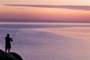 Silhouette of man with fishing spinning. Fishing on the lake at sunset. Lake Ontario. Rochester, USA