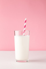 White milk in a glass with straw on a pink background. Modern mockup