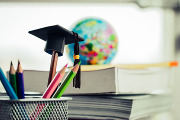 Education Graduate study concept: Black Graduation hat on pencils, blur of europe earth world globe on stack textbook at university classroom. Ideas knowledge learning success, Back to School