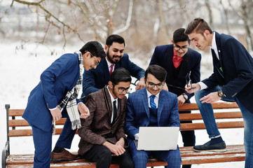 Group of six indian businessman in suits posed outdoor in winter day at Europe, looking on laptop.