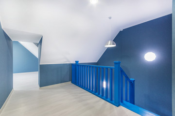 Upper floor room interior with laminate flooring, high ceiling and deep blue wooden staircase.