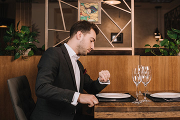 handsome man in suit waiting for girlfriend in restaurant and looking at watch