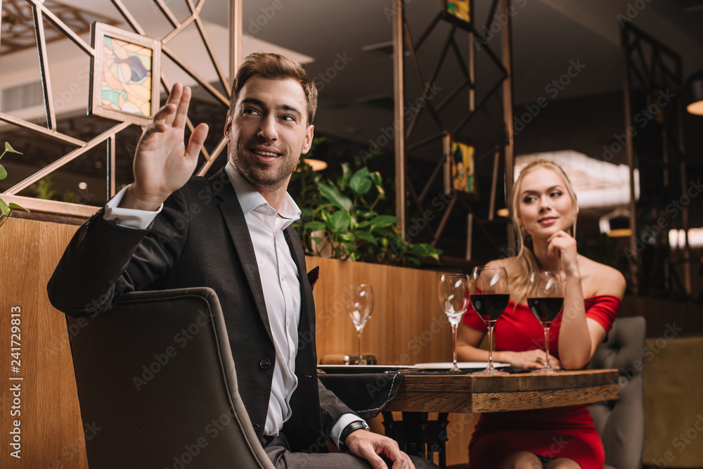 Wall mural handsome man calling waiter while sitting with girlfriend in restaurant