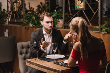 dissatisfied boyfriend looking at girlfriend talking on smartphone during romantic date