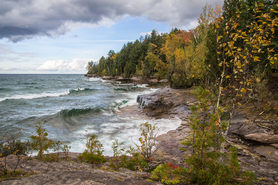 Great Lakes Coastal Landscape. Waves crash on the rocky coast of Lake Superior with fall foliage along the coastal cliffs in Munising, Michigan. 