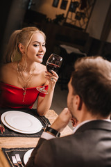 selective focus of attractive woman holding glass with wine and flirting while looking at man in restaurant
