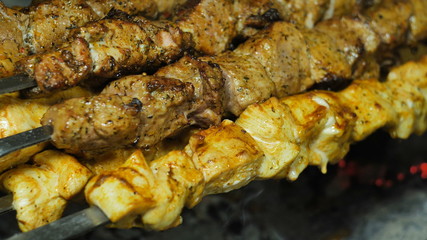 Kebabs of white and red meat strung on a skewer on a grill doused with marinade