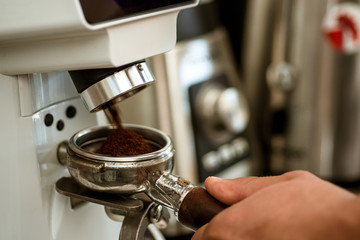 Maximising the freshness. Coffee grinder grinding roasted beans into powder. Fresh ground coffee in portafilter. Barista makes espresso in cafe. Barista grind coffee beans using coffee machine