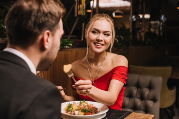 cheerful girlfriend feeding boyfriend in restaurant