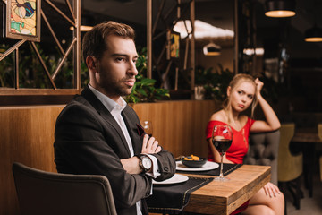 selective focus of man sitting with crossed arms near girlfriend after quarrel in restaurant