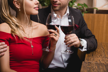 cropped view of man and woman holding glasses with red wine