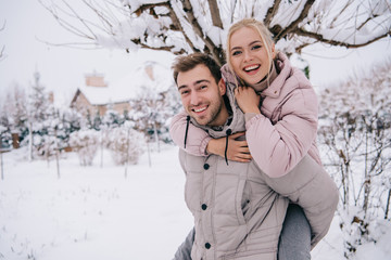 smiling man carrying attractive blonde woman on back in winter