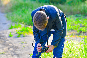 A boy with a camera walks down the street and takes pictures of wild flowers.