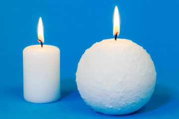Obraz na płótnie Canvas Two white burning candles on blue