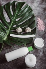  White cosmetic products,  sea salt and  green leaf on gray concrete background . Natural beauty products for skin care. Beauty concept and health. Place for text