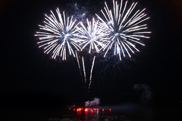 fireworks launched from a riverboat. bright colored explosions in the sky.