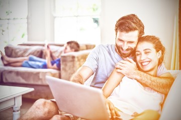 Happy couple sitting on sofa and using laptop