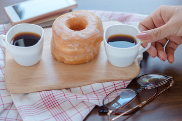 Woman pick cup of coffee on table by sugar donuts