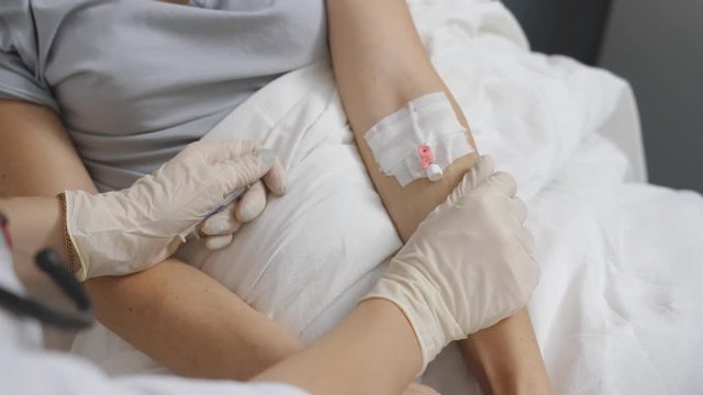 Nurse putting a drip into the catheter lying patients close-up
