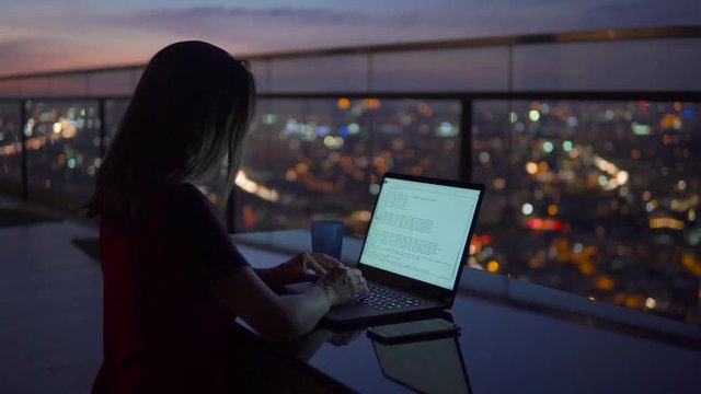 Young Businesswoman work on notebook computer on the balcony of a skyscraper on the background of a fascinating sunset and a view of the night city