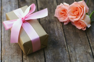 Lovely soft orange pink color rose tied by pink ribbon and brown gift box on wood table background, sweet valentine present concept