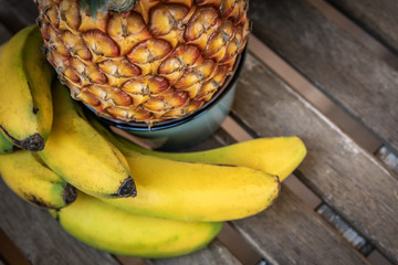 View from the top of a wooden table with pineapple and bananas. Close up food image with tropical yellow and orange fruit. Composition of a group of fruits ananas and platanos Vegetarian healthy foods