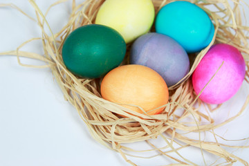 Colorful easter eggs wrapped in raffia nest on white background