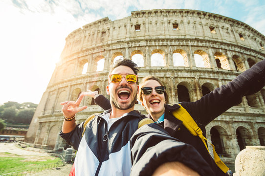 Happy caucasian couple is taking a selfie smiling at the camera in front of the colosseum in Rome