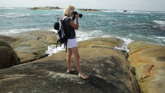 Woman photographer pointing her camera at the sea skyline of Waterfall Beach in Denmark, Western Australia. William Bay national park.