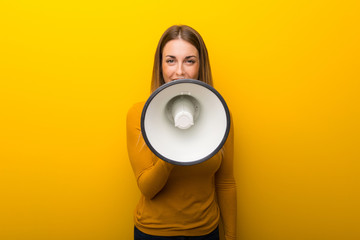 Young woman on yellow background shouting through a megaphone to announce something