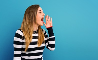 Blonde youn girl shouting with mouth wide open on blue background