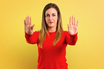 Young blonde woman making stop gesture with her hand on yellow background