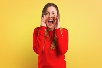 Young blonde woman shouting with mouth wide open on yellow background