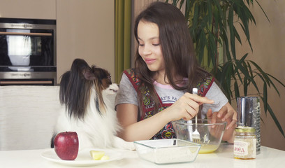 Teen girl with dog Papillon prepare cookies, knead the dough