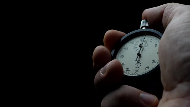 Analogue stopwatch in hand on the black background. Time start with old chronometer. Man presses start button in the sport concept