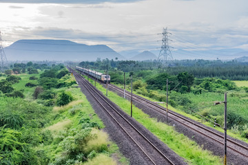 straight railway track goes to horizon in green landscape under blue sky with clouds.