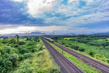 Fototapeta na wymiar straight railway track goes to horizon in green landscape under blue sky with clouds.