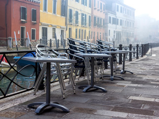 View to a closed restaurant in the foggy canals and streets of Venice