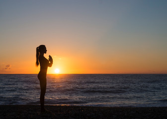 Fototapeta na wymiar Young woman in a meditating yoga pose overlooking the beautiful sunset. Mind body spirit concept.