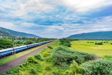 awesome view of indian railway running on track goes to horizon in green landscape under blue sky with clouds.