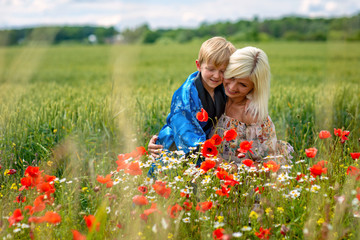 Mom with her son in a magnificent meadow. The boy surprised her mother with red poppies.