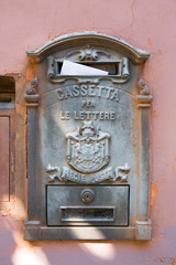 Vintage Italian mailbox (Cassette per le Lettre) with white envelope on a light red plastered wall.