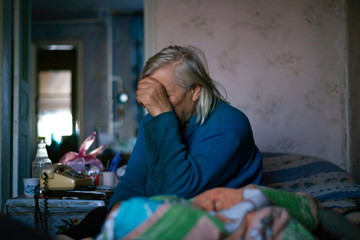 Old poor gray hair woman covered her face with her hand. Woman is sad. Poor life in village. Old age not good. Low-light photo.
