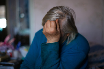 Old poor gray hair woman covered her face with her hand. Woman is sad. Poor life in village. Old age not good. Low-light photo.