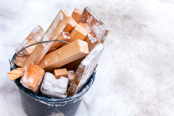 Bucket full of firewood standing on snow.