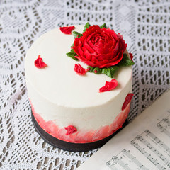 White cream cake decorated with red buttercream rose on a wooden background with lace fabric. It is suitable for parties in festivals of happiness such as Valentine's Day, Mother's Day,Birthday party.