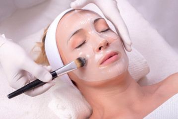 Beautiful woman during beauty skin mask treatment on her face with brush
