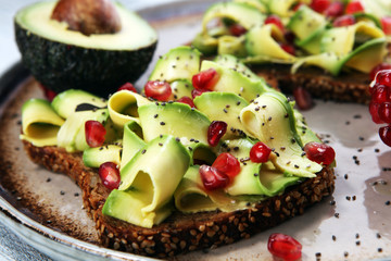 sliced avocado and ripe pomegranates on toast bread with spices and avocado.